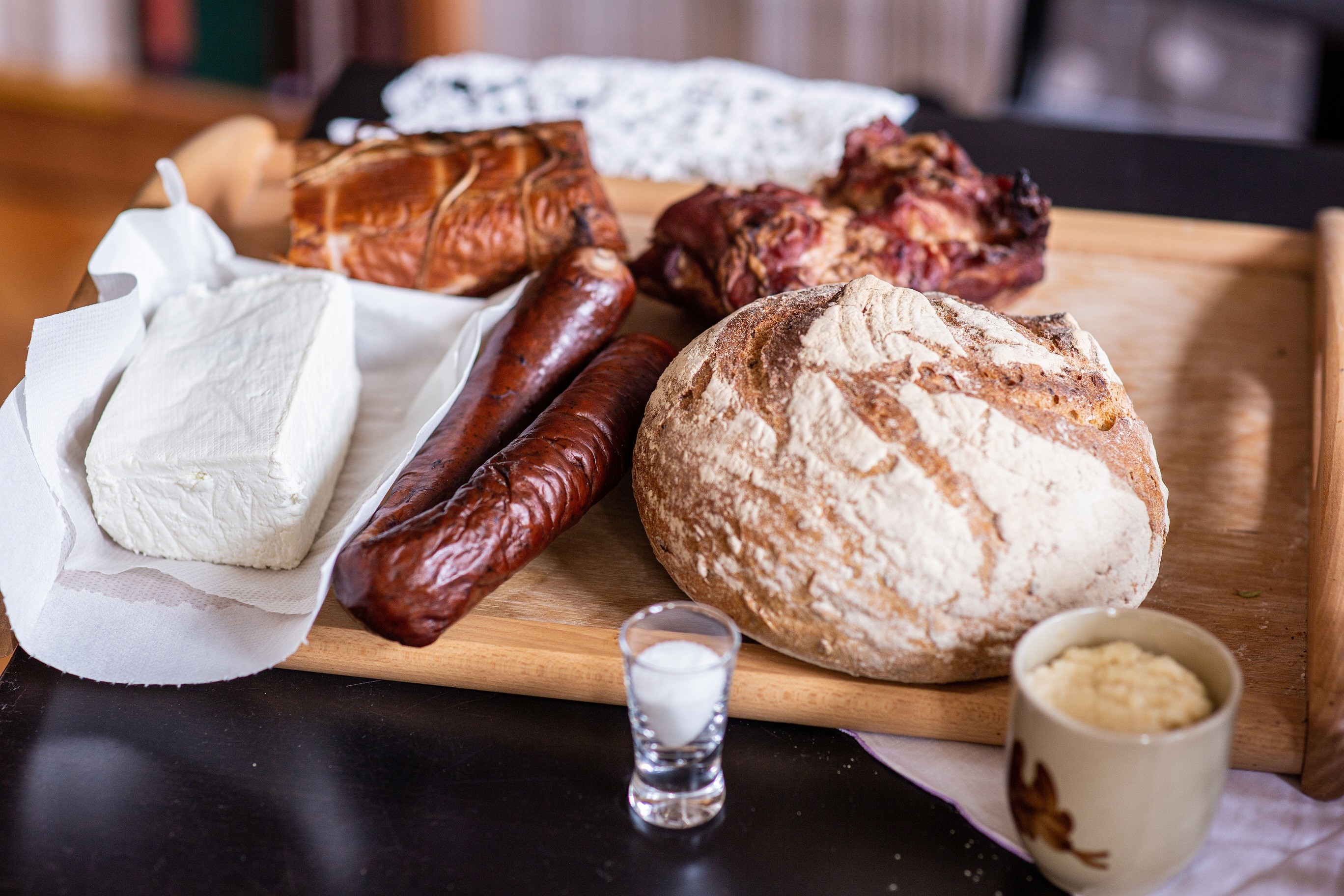 biały ser, kiełbasa, chleb, chrzan, i sól ułożone na desce do krojenia 